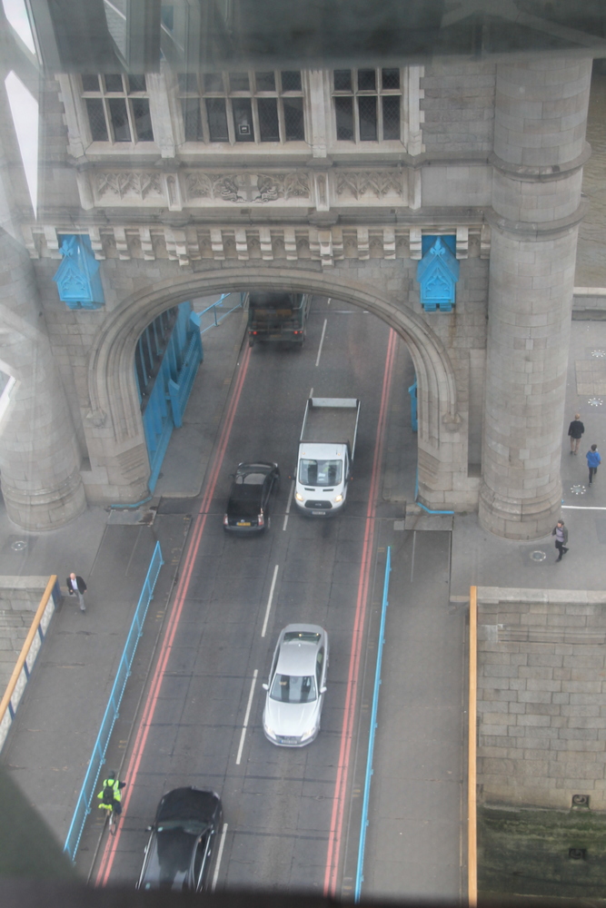 !Widok (przez przeszkloną podłogę) z kładki Tower Bridge na jezdnie mostu