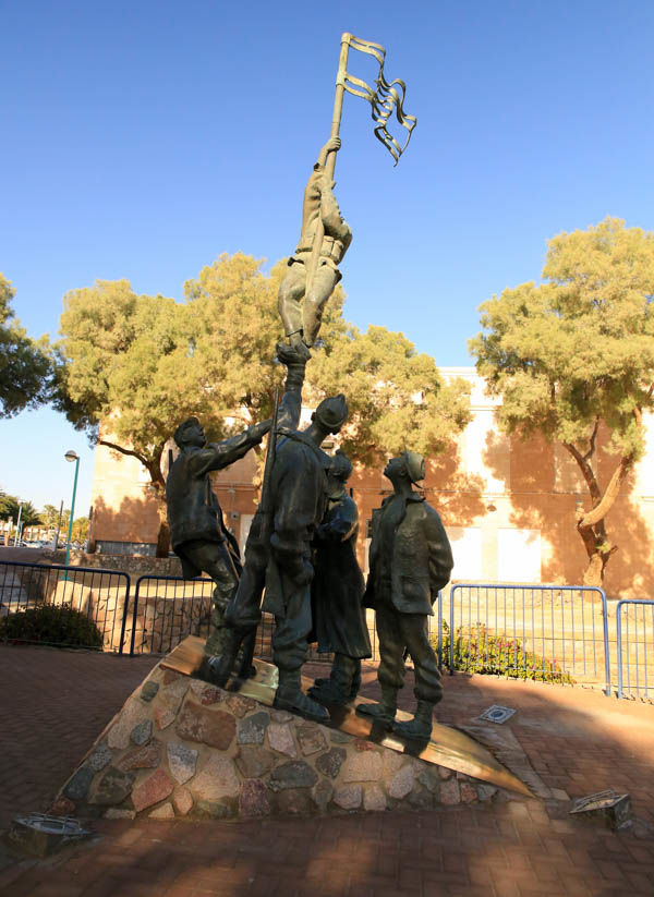 !Monument przedstawiający żołnierzy izraelskich wznoszących maszt z flagą obok pamiątkowego posterunku w Ejlacie